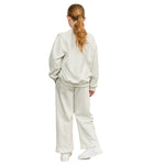 A woman viewed from behind wearing a matching light heather gray sweatshirt and wide-leg sweatpants set, paired with white sneakers, against a plain white background.