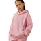 A young girl wearing a light pink oversized hoodie sweatshirt with a small embroidered  logo on the chest, set against a plain white background.
