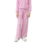 A person wearing a pink ribbed lounge set with a matching long-sleeve top and wide-leg pants, paired with white sneakers, shown against a plain white background.