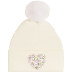An off-white ribbed knit pom-pom beanie featuring a pink and green floral heart patch on the front cuff.