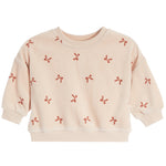 A light beige crewneck sweatshirt with long sleeves, featuring an all-over pattern of small red ribbon bows, shown against a plain white background.