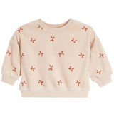 A light beige crewneck sweatshirt with long sleeves, featuring an all-over pattern of small red ribbon bows, shown against a plain white background.