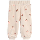 A pair of cream-colored fleece pants with a repeating pattern of small red bows, featuring an elastic waistband and ribbed ankle cuffs.