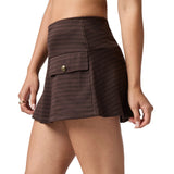 A model wearing a brown houndstooth mini skirt with a front flap pocket and a gold button, shown from the waist down on a white background.