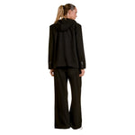 A woman shown from the back wearing a black hooded blazer and matching wide-leg trousers against a plain white studio background.