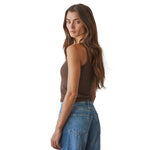 A woman with long brown hair is shown from a side-back angle wearing a fitted brown ribbed tank top and blue jeans against a plain white background.