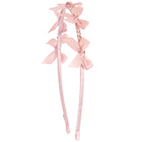 A light blush headband decorated with three matching satin bows and small gold rhinestone accents, shown against a plain white background.