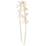 An off-white satin hair accessory featuring three layered bows, rhinestone accents, and a decorative top, attached to two long ribbons on a plain white background.