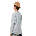 A boy from the back wearing a light gray long-sleeve t-shirt, a tan baseball cap with a white embroidered logo, and dark patterned shorts, set against a plain white background.