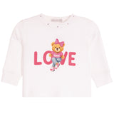 A white long-sleeve baby/toddler top featuring a central graphic of a teddy bear wearing a pink bow and jeans, sitting on the word 'LOVE' in pink letters.