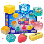 Squishy Fun Box sensory toy set with a blue retail box and multiple toy pieces including a yellow cheese cube, translucent blue ice cubes, a pink apple, a bread loaf, a strawberry, butter, and other textured food-like shapes, arranged on a white background with small star confetti.