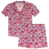 A two-piece short-sleeve pajama set with a vibrant multicolor floral print on a pink base, featuring a matching collared top and shorts.
