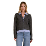 A woman modeling a dark charcoal cable-knit zip-front cardigan with light blue shirt-collar and hem details against a plain white background.