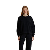A woman modeling a black crewneck sweatshirt and matching black sweatpants against a solid white background.