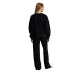 A woman with long light brown hair is shown from the back wearing a matching black sweatshirt and wide-leg sweatpants set, standing against a solid white background.
