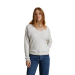A woman with red hair wearing a light heather gray v-neck sweater and blue jeans, standing against a solid white background.