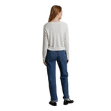 A woman shown from the back wearing a light gray long-sleeve knit sweater and blue jeans, standing against a plain white background.