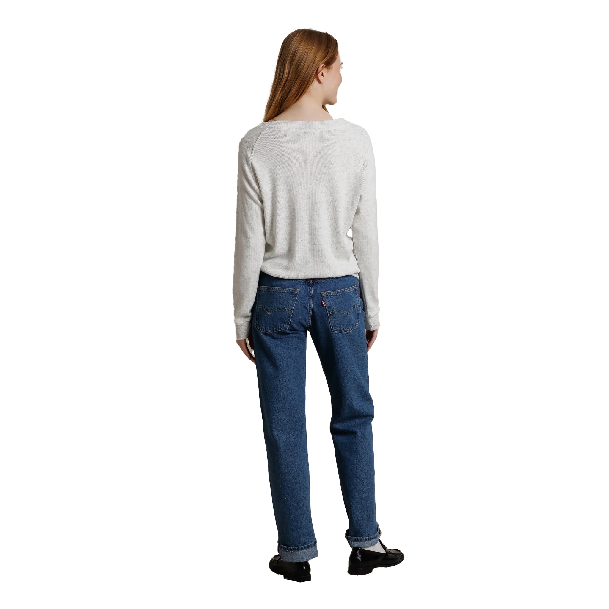 A woman shown from the back wearing a light gray long-sleeve knit sweater and blue jeans, standing against a plain white background.