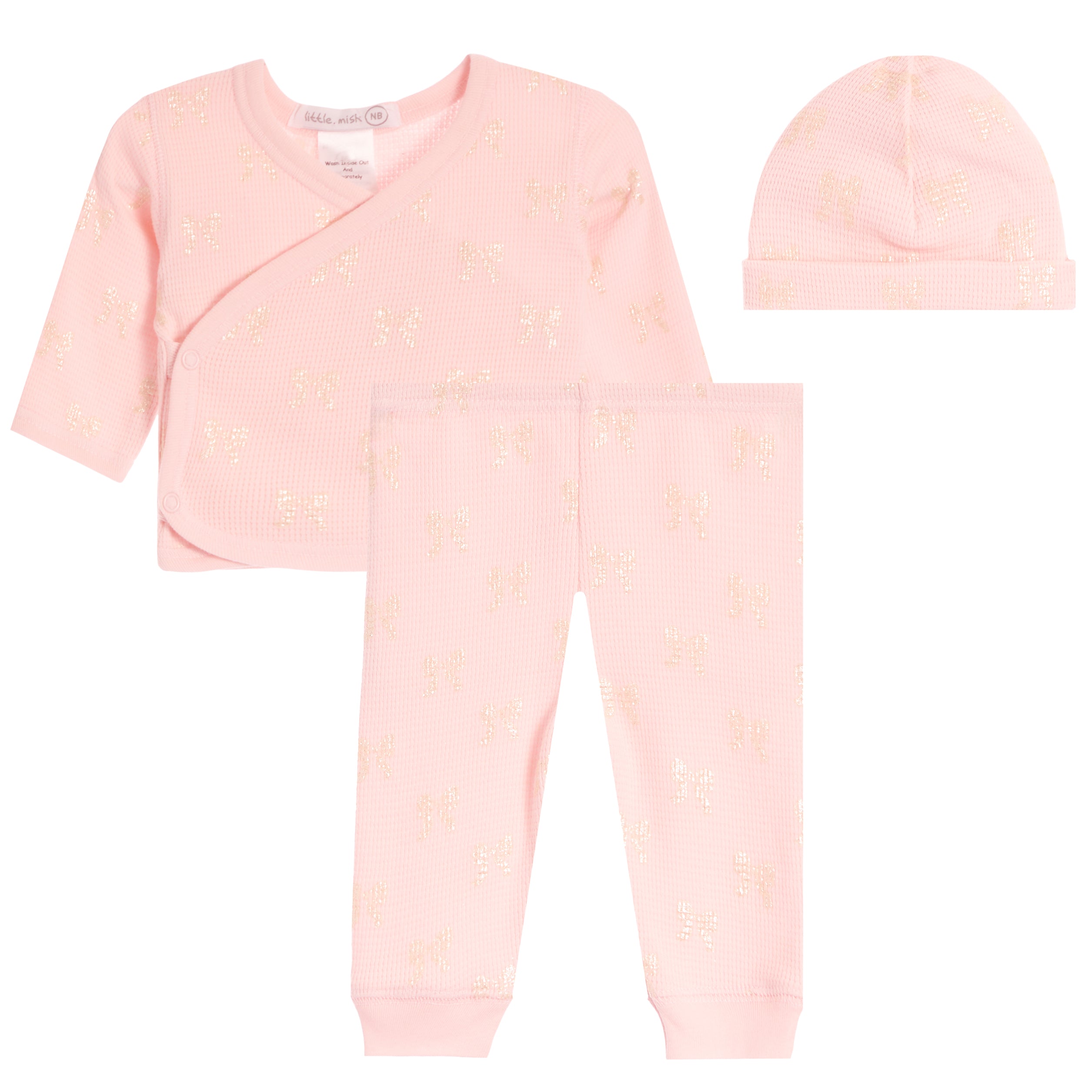 A three-piece baby clothing set in light pink, featuring a long-sleeve wrap top, matching pants, and a knit beanie, all decorated with a subtle metallic gold bow pattern.