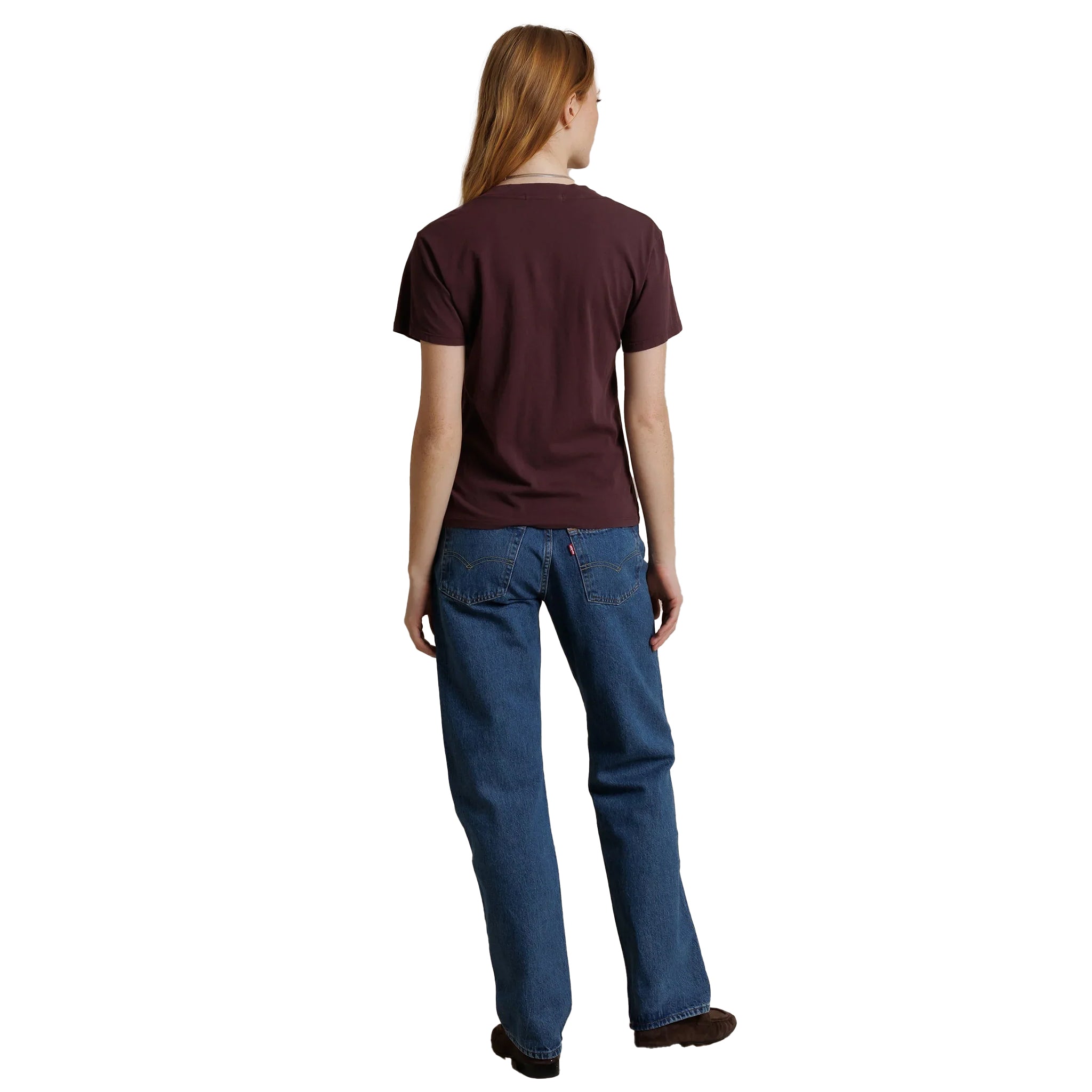 A woman viewed from behind wearing a short-sleeve crewneck t-shirt in maroon and blue jeans, standing against a plain white background.