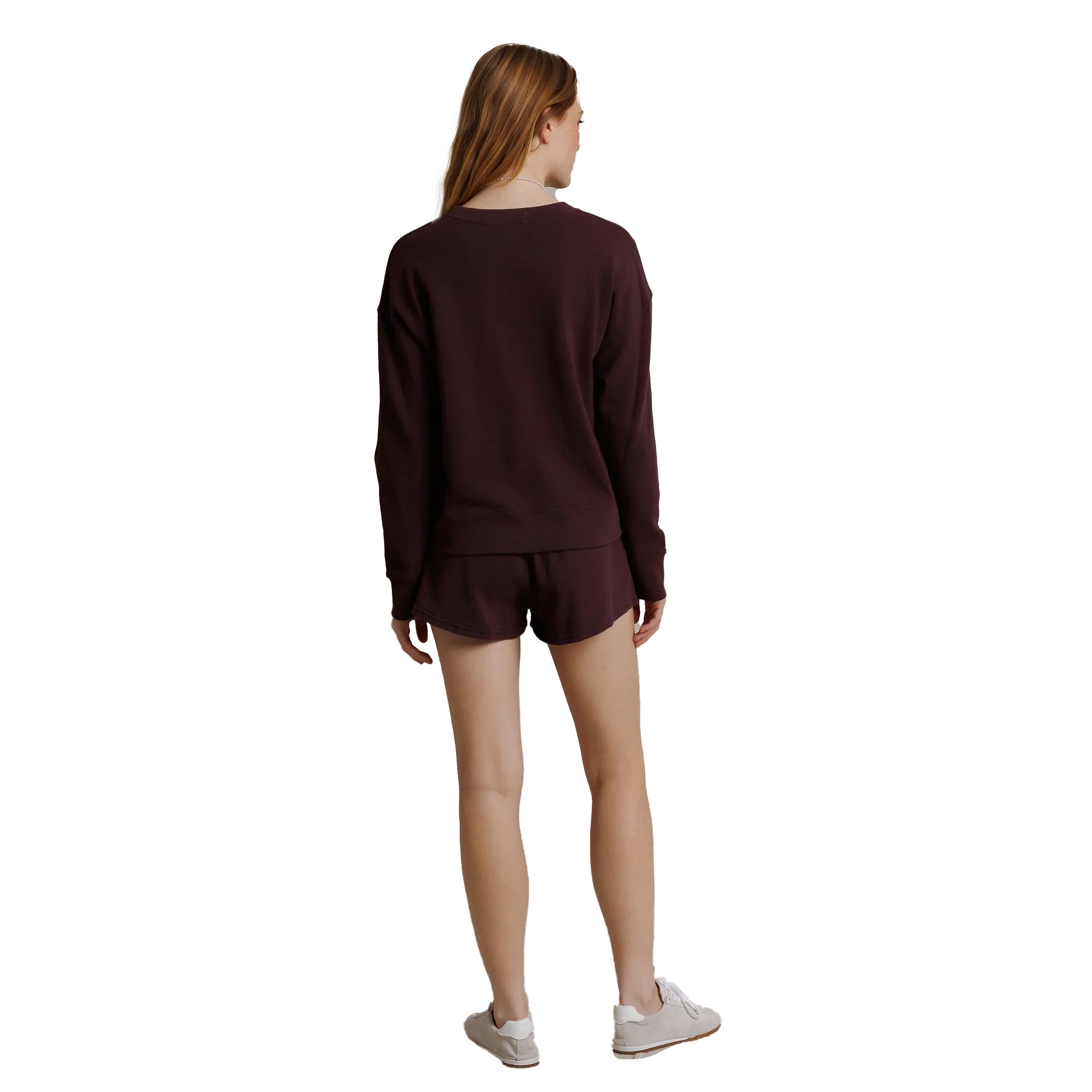A woman shown from the back wearing a matching dark burgundy long-sleeve top and shorts set, paired with white sneakers, against a plain white background.
