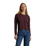 A woman modeling a dark burgundy long-sleeve crop top with blue jeans against a plain white background.