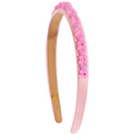 A light pink plastic headband decorated with a row of small pink and lavender flower charms and rhinestones on the outer band, shown against a plain white background.