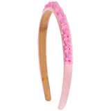 A light pink plastic headband decorated with a row of small pink and lavender flower charms and rhinestones on the outer band, shown against a plain white background.