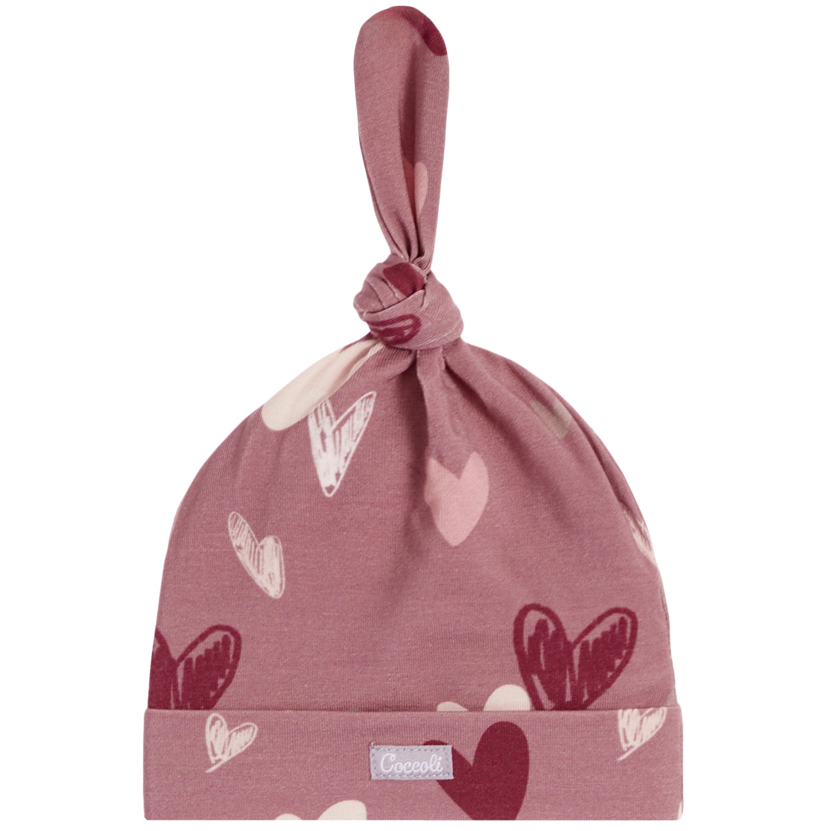 A dusty rose knit baby hat with a knotted top and a folded cuff, decorated with a pattern of hearts in various shades of pink, red, and white. A small silver brand tag is visible on the cuff.