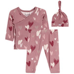 A baby clothing set featuring a dusty rose long-sleeve wrap shirt, matching leggings, and a knotted beanie hat, all printed with a heart pattern in shades of pink, red, and white. 