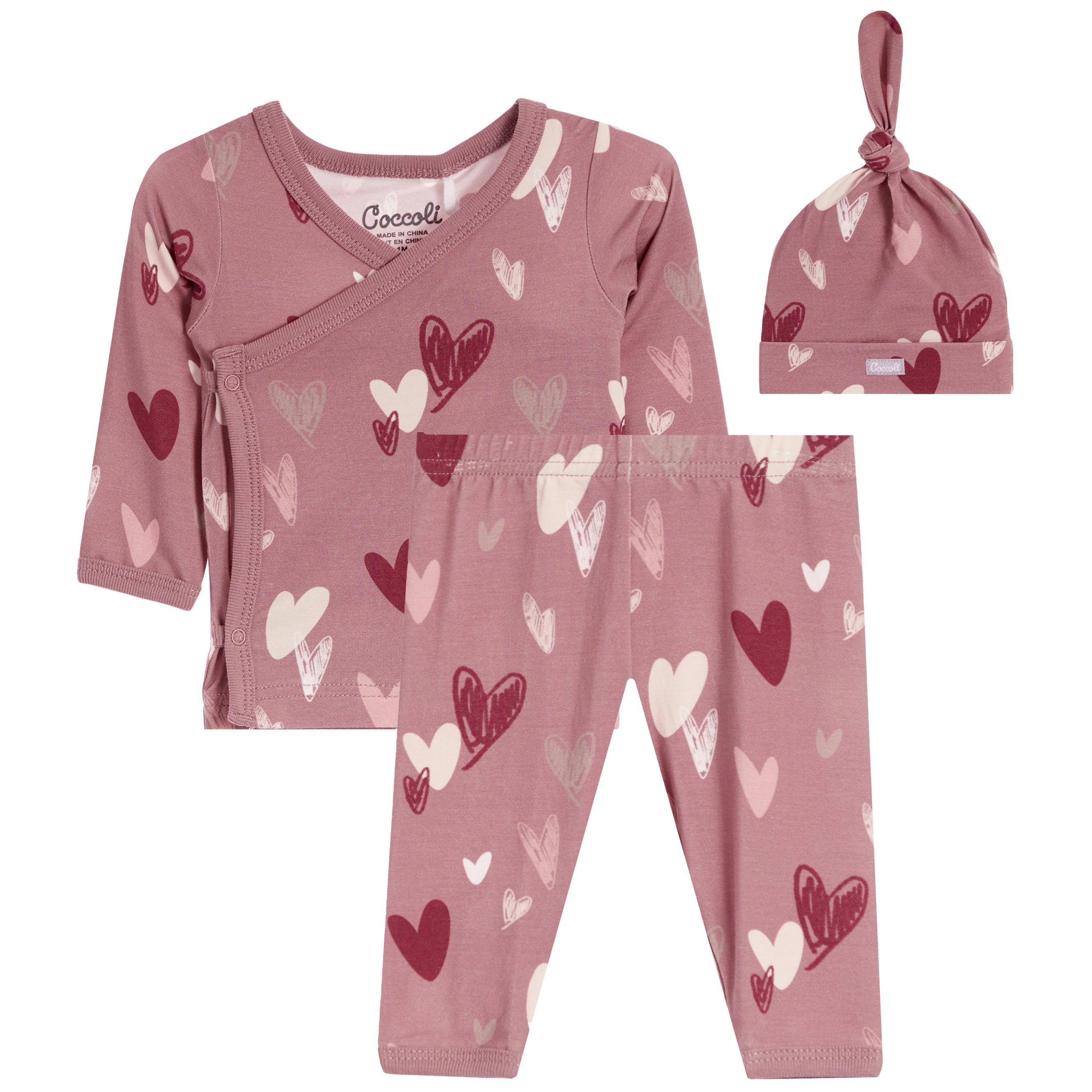 A baby clothing set featuring a dusty rose long-sleeve wrap shirt, matching leggings, and a knotted beanie hat, all printed with a heart pattern in shades of pink, red, and white. 