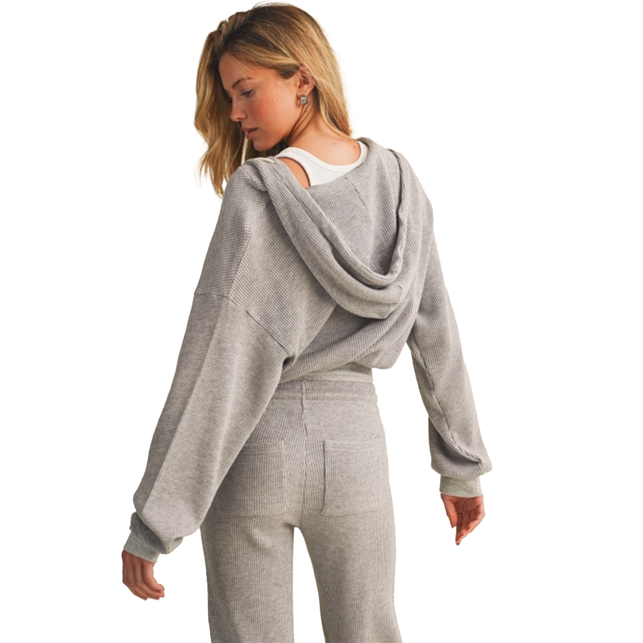 A woman wearing a light gray heathered cropped hoodie with a draped hood and matching jogger pants, shown from a back three-quarter view against a plain white background.
