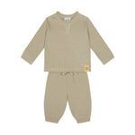 A two-piece baby loungewear set in a warm beige waffle-knit fabric, featuring a long-sleeve top with a small yellow brand patch on the sleeve and matching pants with a drawstring waist.