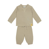 A two-piece baby loungewear set in a warm beige waffle-knit fabric, featuring a long-sleeve top with a small yellow brand patch on the sleeve and matching pants with a drawstring waist.