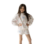 Young girl wearing a white hoodie and shorts set with pink floral patterns and blue 'happy camper' text on a white background