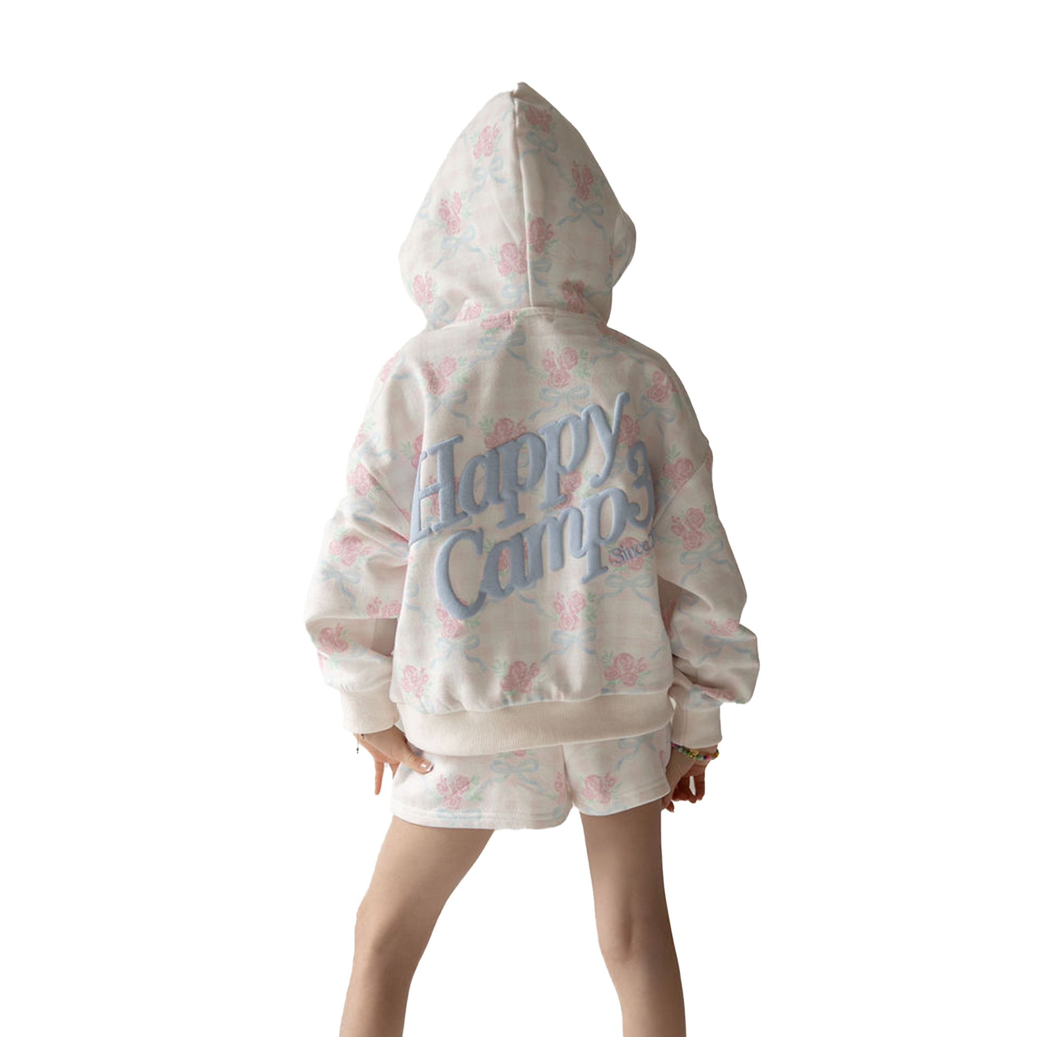 Young girl wearing a white hoodie and shorts set with pink floral patterns and blue 'happy camp' text on a white background