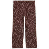 A pair of dark brown pants featuring a small, repeating beige abstract floral pattern, shown flat against a solid white background.