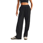 A person modeling black wide-leg sweatpants with a matching black waistband and white piping, paired with a black-and-white striped crop top and white sneakers, against a plain white background.