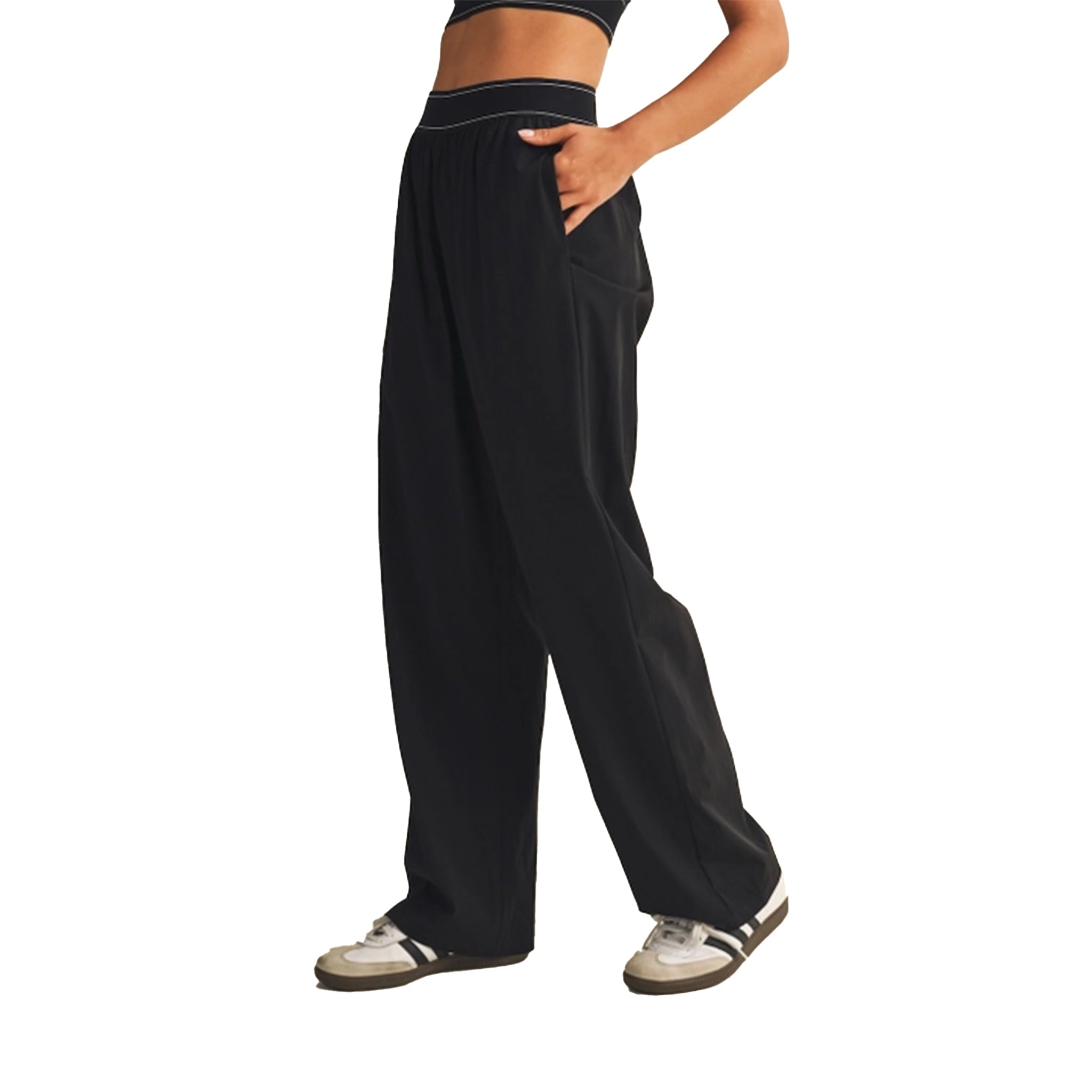 A person wearing loose black wide-leg sweatpants with side pockets, paired with white sneakers, shown from the waist down against a plain white background.