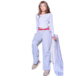 A young girl modeling a white long-sleeve crop top, grey sweatpants, a red plaid belt waistband and beige slip-on shoes, holding a sheer white lace fabric against a plain white background.
