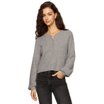 A woman wearing modeling a cropped, long-sleeve henley-style knit top in grey dark gray jeans against a plain white background.