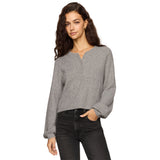 A woman wearing modeling a cropped, long-sleeve henley-style knit top in grey dark gray jeans against a plain white background.