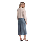A woman shown from the back wearing a light beige cropped cardigan and a slate blue midi skirt, paired with black mule sandals, against a plain white background.