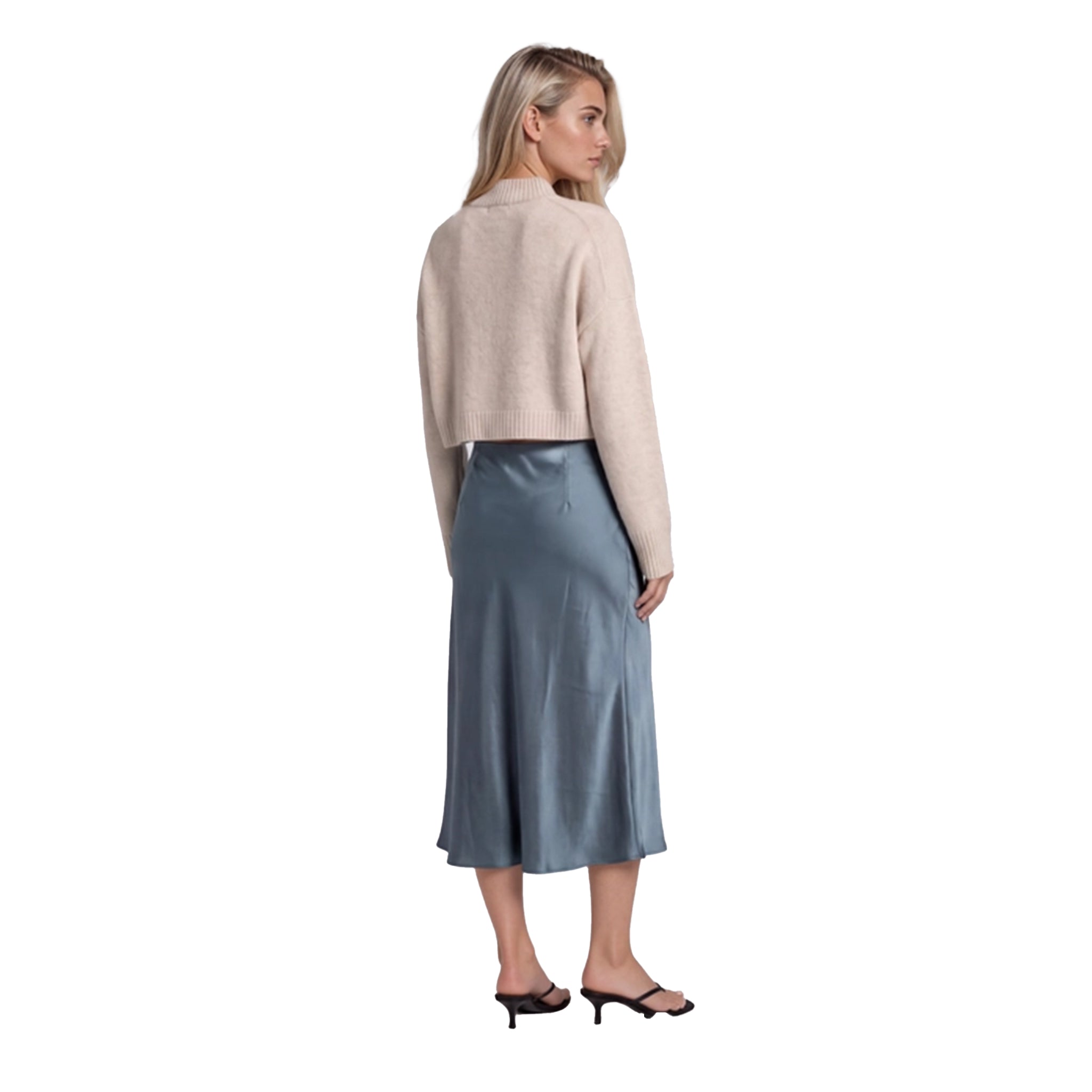 A woman shown from the back wearing a light beige cropped cardigan and a slate blue midi skirt, paired with black mule sandals, against a plain white background.