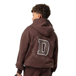 A child model shown from the back wearing a dark brown cropped hoodie with a large white outlined letter 'D' and the words 'DRIP ATHLETIC DEPT. ESTABLISHED 2023' printed on the back, paired with matching brown sweatpants against a plain white background.